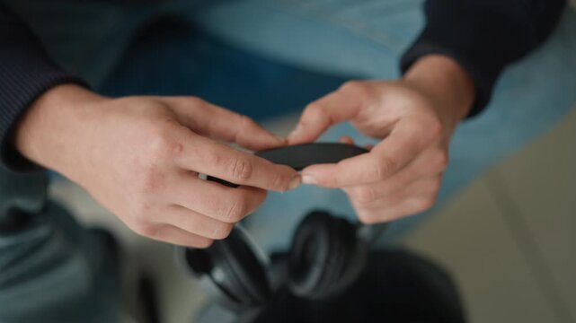 Close up of hands holding and adjusting black headphones focusing on texture detail. Hands manipulate headphone band with visible skin textures like calluses or scars. Background shows