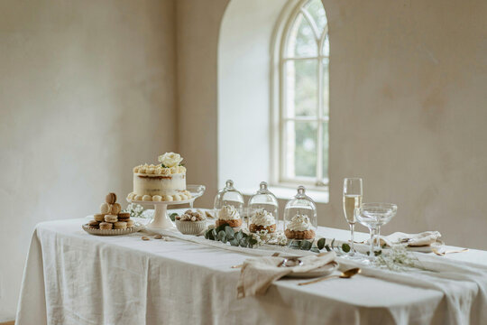 Elegant white wedding cake and dessert table setup near church window with interior
