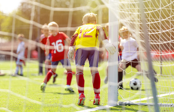 View Through Goal Netting of Junior Soccer Players Attacking and Defending Near Goal Box - Youth Football Match Action on Grass Pitch
