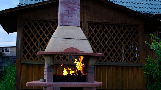 Rustic cottage, cozy outdoor BBQ zone. A warm fire burns inside the traditional stone oven, creating an inviting atmosphere. Authentic rural scene, charm of country living,  vacation away from  city. 
