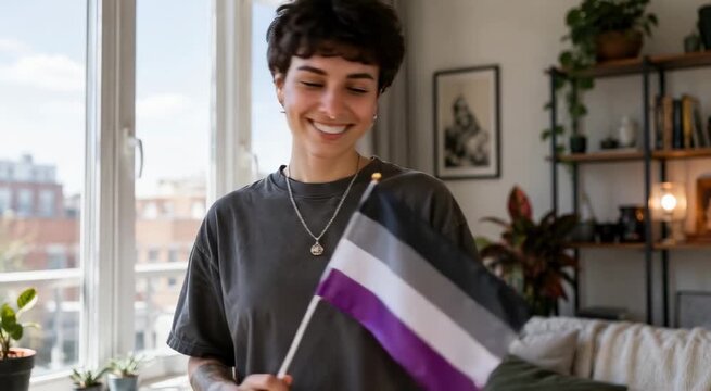 Smiling young person indoors holding an asexual pride flag in a cozy, plant-filled living room