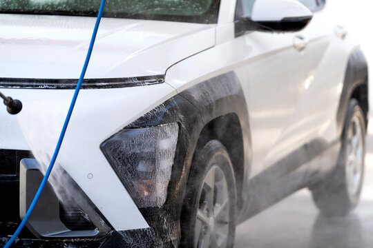 Car washing a white suv with a high-pressure hose at a self-service station