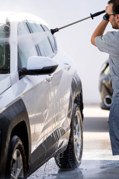 Young man washing car with pressure washer at self-service car wash station