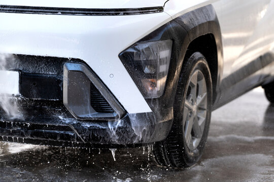 Washing white suv at car wash station with high-pressure water and foam soap