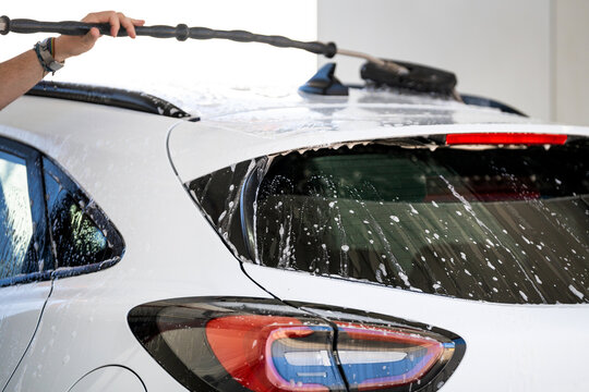 Young man washing white car with a brush at a self-service pressure wash station