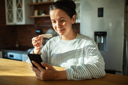 Smiling woman holding positive pregnancy test in home kitchen
