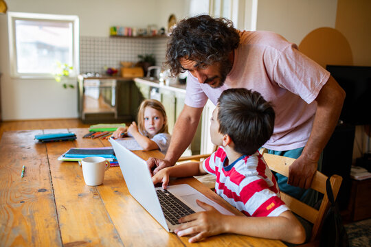 Father helping son with homework on laptop at kitchen table