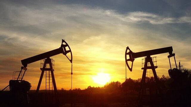 View of oil pump jacks operating in an oil field during a golden sunset in Russia.