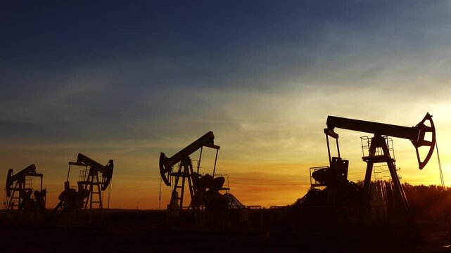 View of oil pump jacks silhouetted against a vibrant sunset sky in Russia.
