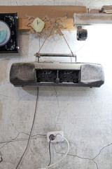 Old boom box hanging on a wall in a room with peeling paint near a clock and a power outlet © indigolotos
