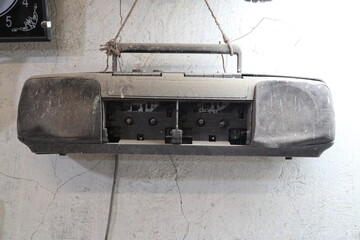 Old boom box hanging on a wall in a room with peeling paint near a clock and a power outlet © indigolotos