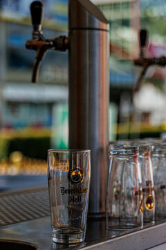 Neuwied, Germany - July 10, 2026: Row of empty Benediktiner Hell branded beer glasses, including a , lined up on a bar counter with two beer taps ready for service in an outdoor setting