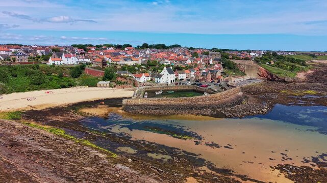 Aerial view of Crail Harbour, sandy Crail Beach, stone pier, and coastal village on the Fife coast of Scotland, United Kingdom. 4K UHD video.