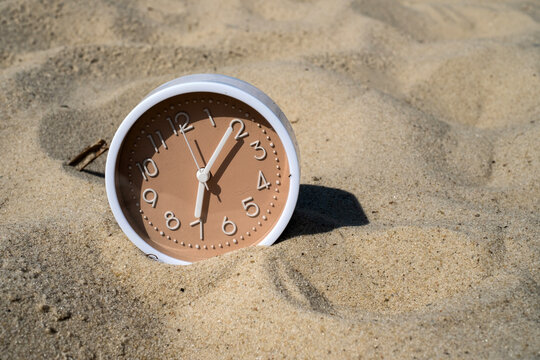 Modern beige clock buried in beach sand for time slow living vacation countdown and relaxing summer concept	
