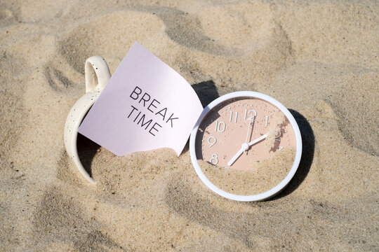 Coffee cup with BREAK TIME card and beige clock buried in beach sand for time is up and vacation end concept