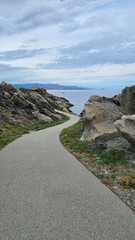 Obraz premium Curving coastal asphalt path leading through rocky cliffs near the sea
