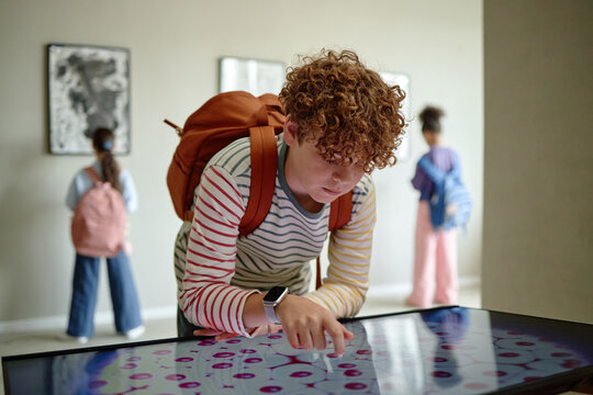 Caucasian teenager boy using interactive digital screen in art gallery during school field trip. Image suitable for promoting modern museum education programs