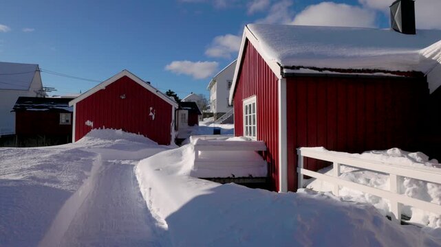 View of traditional red rorbuer cabins surrounded by deep snow under a clear blue sky in Hamnoy, Nordland, Norway.