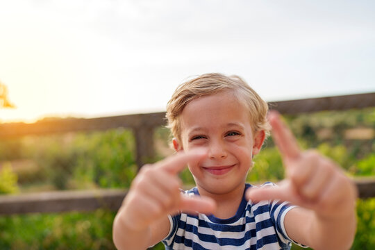 Happy child framing the view with his fingers, finding new vision and creativity, looking at the camera