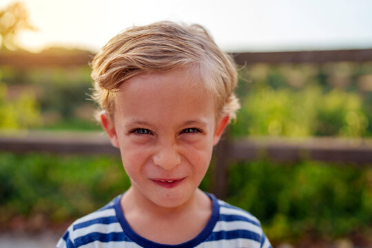 Young boy making a funny grimace looking directly at camera, expressing childhood joy and playfulness outdoors