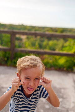 Young boy making funny face pulling cheeks and sticking out tongue expressing playful childhood emotion