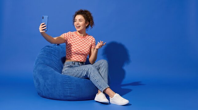 Happy Young Woman Taking Selfie on Smartphone While Relaxing on Bean Bag Chair.