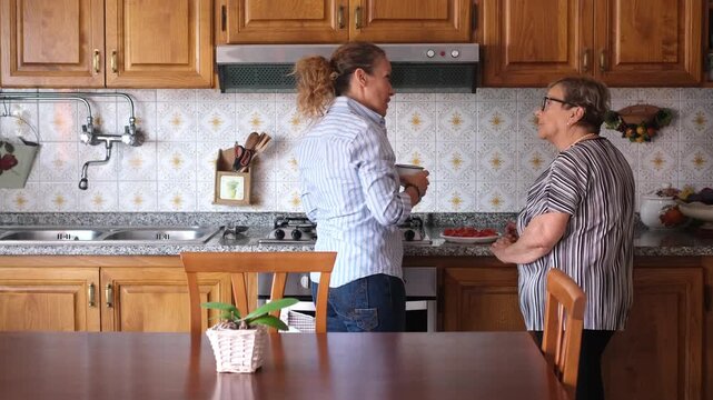 Joyful adult daughter and her elderly mother happily dancing and having fun together in their home kitchen, representing family love, bonding, and intergenerational connection