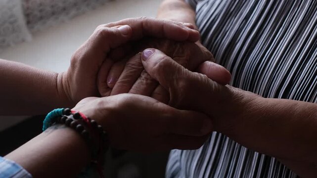 Close-up of a younger person's hands gently holding and comforting the wrinkled hands of an older woman, symbolizing compassion, family love, generational connection, and support