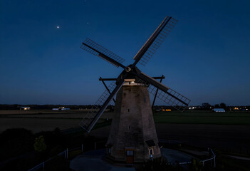 Obraz premium Renewable energy and sustainability, historic windmill in rural landscape at twilight with starry sky and agricultural fields for green power