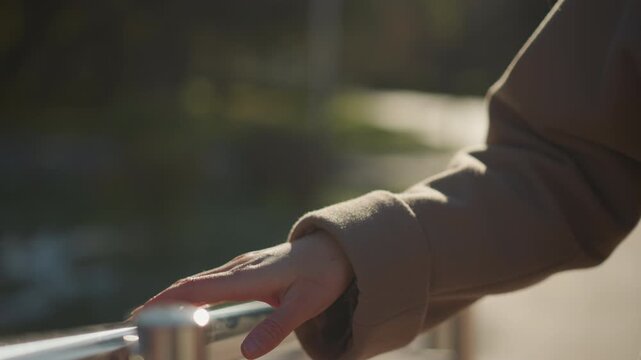 Close up of woman hand resting on and gently tracing along polished metal railing. soft sunlight highlights skin texture casting subtle shadows that emphasize movement across smooth surface