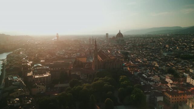 Golden aerial panorama glides past Basilica Santa Croce toward Palazzo Vecchio, the Duomo and hazy Tuscan hills at sunset.
