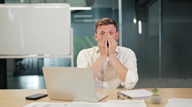 Professional man experiences significant work-related stress. Demonstrating feelings of exhaustion, frustration, and potential burnout, struggling with office demands and tasks at desk.