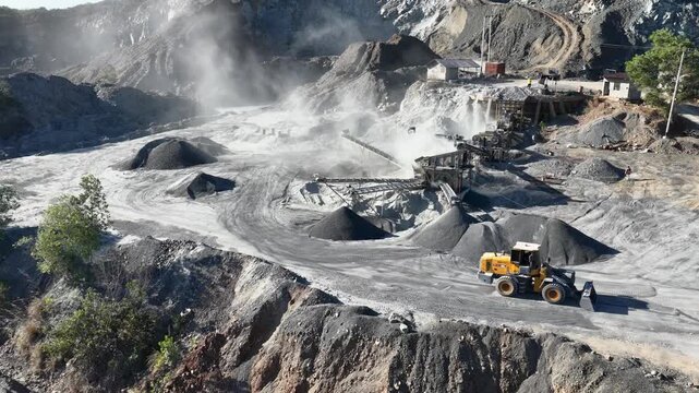 Yellow loader moving gravel piles at a busy industrial stone crushing and mining site