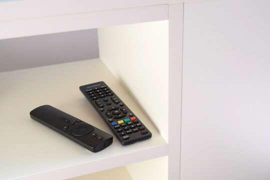 Two black TV remote controls on a white shelf of a modern media unit