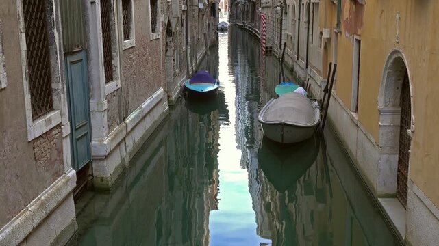 View of a narrow canal with moored boats and historic buildings in Venice, Veneto, Italy.