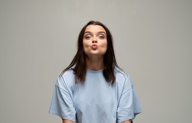 Fototapeta premium Young woman making a kissing face playfully pouting lips in a studio portrait with gray background
