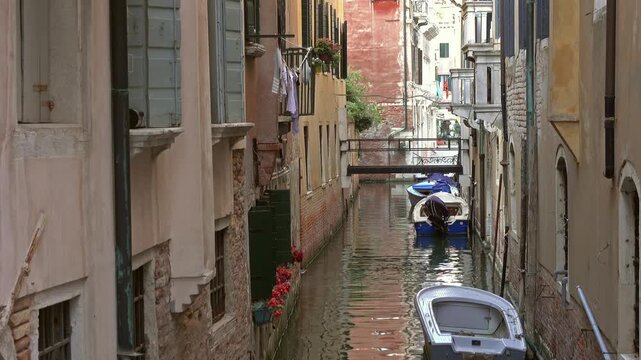 View of a narrow canal lined with historic buildings and small boats in Venice, Veneto, Italy.