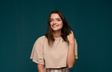 Obraz premium Young brunette woman posing with a cheerful smile, touching her hair, conveying casual style and positive feelings