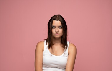 Young woman looking directly at camera with a serious or concerned expression on a pink background,...