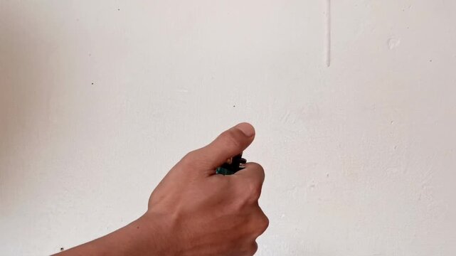 A human hand strikes a match to produce a small flame in a room with a plain white background.