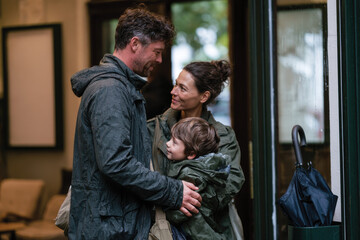 Obraz premium A family shares a joyful embrace outside a building in the rain, capturing a moment of affection and unity amid the elements.