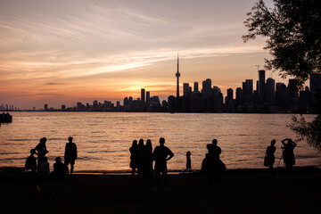 Fototapeta premium Toronto skyline with CN Tower at sunset, silhouettes of people by Lake Ontario waterfront. g.