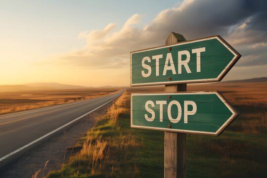 Wooden road sign displaying start and stop directions along a scenic rural highway at sunset