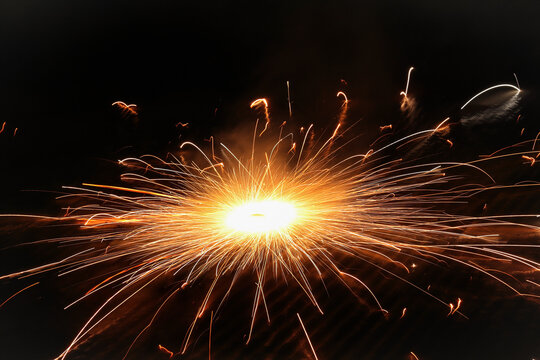 Sparkling Diwali Ground Chakra Firework Spinning at Night: Long Exposure Photo of Glowing Golden Sparks, Traditional Festive Indian Firecracker Light Display Isolated on Dark Black Background