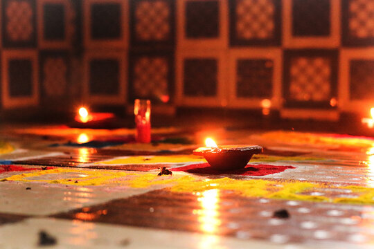 Lit Clay Diya on Colorful Rangoli Design, Traditional Oil Lamp with Burning Flame on Floor Decoration for Indian Festival of Lights Diwali, Deepavali Celebration Background, Low Angle Macro Shot