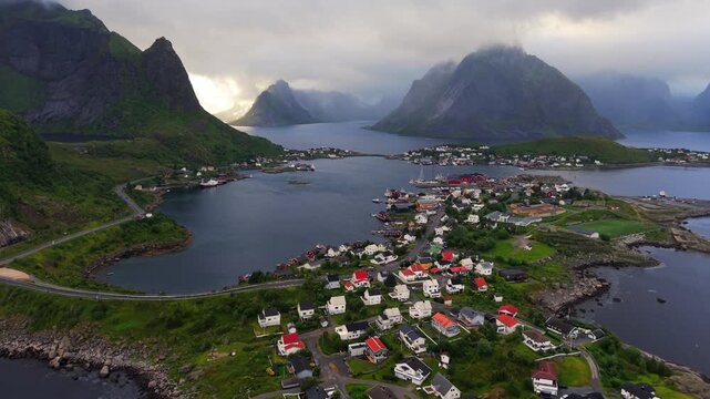 Aerial view of Reine fishing village in the Lofoten Islands, Norway, surrounded by dramatic mountains, calm fjord waters and small coastal settlements beneath a moody Arctic sky