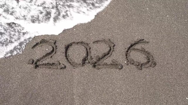 Sea wave erasing the year 2026 written on dark sand beach