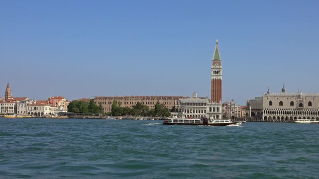 View of St. Mark's Campanile and the Doge's Palace seen from the water with a boat passing by in Venice, Veneto, Italy.