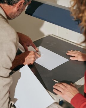 Hands of two people comparing documents on a dark desk under a task light, featuring a tactile matte surface for election integrity and scrutiny