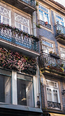 Faded Artificial Flower Display Covering a Shopfront Cornice Below an Iron Balcony, Porto, Portugal — Concept: Retail Visual Merchandising, Weathered Decoration and Street Detail © Svetlana